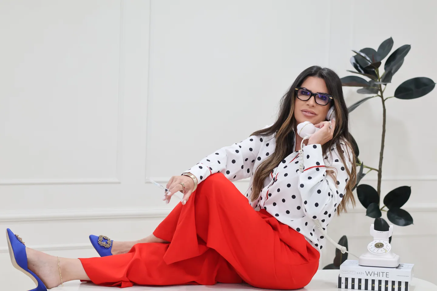 Eileen Rivera Jimenez holding a white telephone in a polka-dot blouse and red trousers.